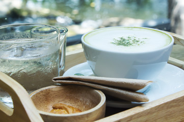Hot green tea latte with matcha powder on wooden background.