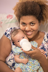 Happy african american mother bottle feeding her mixed race baby daughter