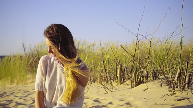 Girl spending free time on seashore. Young long hair woman enjoying windy summer day on sandy beach dunes 4K ProRes HQ codec