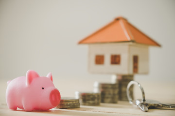Pig money box and paper house with key on wooden wall background