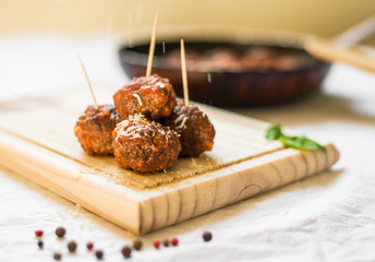 Meatballs in tomato sauce on a wooden board with toothpicks against white background