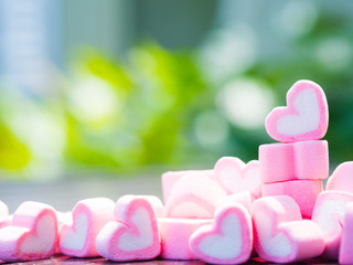 Closeup of sweet marshmallow in the shape of heart on wooden plate and flower at background....
