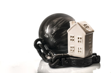 Fototapeta premium Debt burden and mortgage make you a slave concept with a ball and chain and a house next on white background