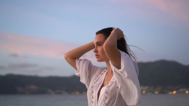 Closeup portrait of sensual woman in white linen dress posing on the sandy beach on tropical paradise island with beatiful summer sunset sky - video in slow motion