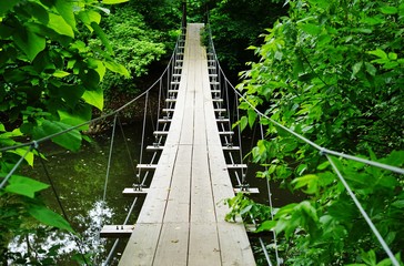 Small wood pedestrian suspension bridge with steel cables over a river in the woods