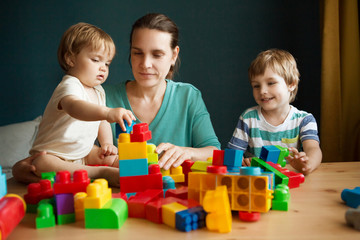 mother and children  playing with lots of colorful plastic blocks constructor indoor.  The happy family spends time together at home.