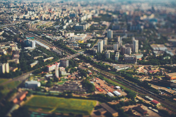 Fototapeta na wymiar True tilt-shift view from very high above of railway with several tracks, aerial view of railroad station in focus surrounded by defocused residential districts and industrial zone, Moscow, Russia