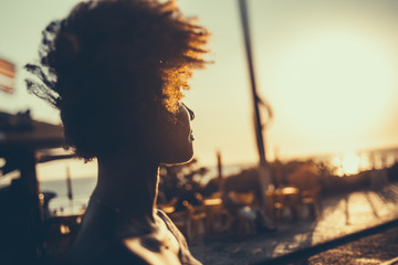 Silhouette of young Brazilian girl with curly afro hair illuminated by orange light looking on...