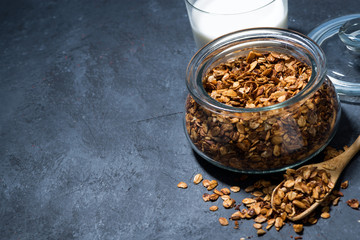 homemade baked granola in a glass jar and milk on dark background