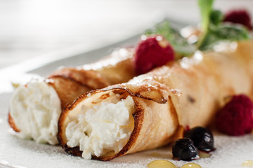 Pancake with cottage cheese close up. Restaurant serving of healthy morning breakfast. Homemade rolled dessert with raspberries on white plate.