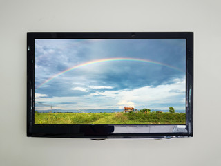 Led tv on the wall background with rainbow in the sky over agriculture field on television screen