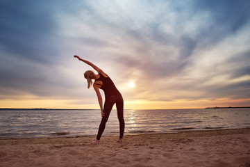 Fototapeta na wymiar young woman exercising on the beach at beautiful sunset