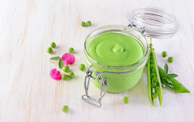 Healthy food. Fresh puree of green peas in open glass jar with pink flowers of sweet pea