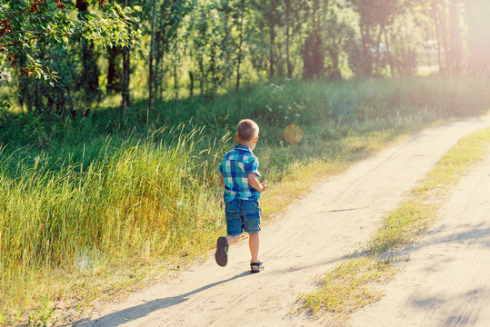 Little boy in a blue plaid shirt and shorts runs on a footpath in the wood