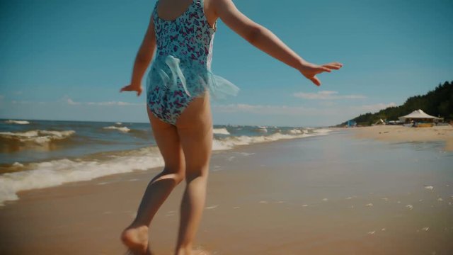small and adorable little girl runs on a beach by the sea in summer