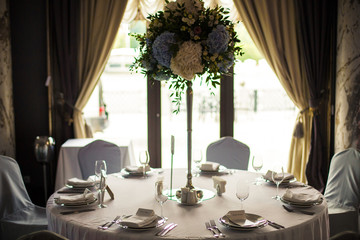 Tall bouquet of blue and white hydrangeas stands in the middle of dinner table