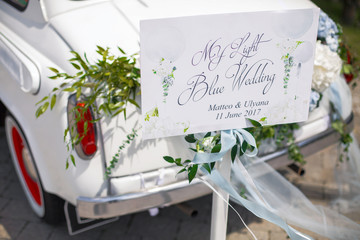Card with lettering 'My light blue wedding' stands before a car on the backyard