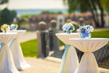 Little tables covered with white cloth and blue flowers stand on the backyard