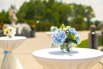 Little bouquets of blue hydrangeas stand on little tables outside