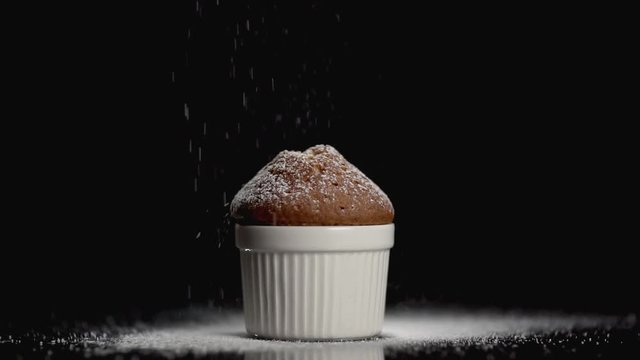 Sprinkle muffin cake with white powdered sugar on black background with copyspace. Slow motion.