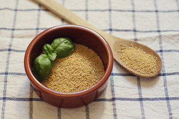 Couscous in a bowl with basil leaves and a wooden spoon
