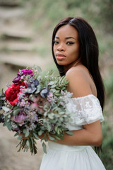 Bride with dark skin holds rich red bouquet in her tender arms