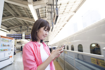 Obraz premium A woman is waiting for a bullet train while watching a smartphone