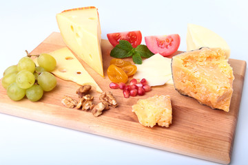 Assortment of cheese with fruits, grapes, nuts and cheese knife on a wooden serving tray.