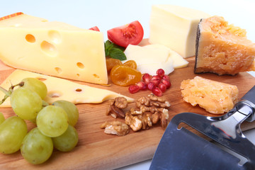 Assortment of cheese with fruits, grapes, nuts and cheese knife on a wooden serving tray.
