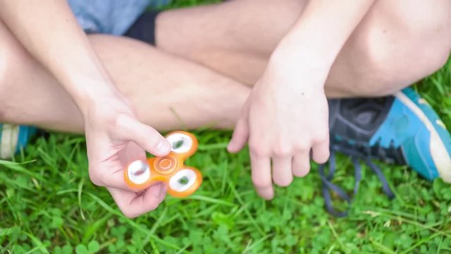 Child having fun outdoors with Spinner. Teen boy showing skills by flicking fidget spinners with finger. Teenager in the summer park.