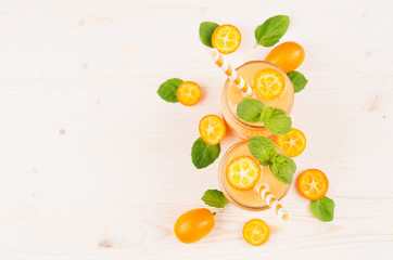 Orange citrus kumquat  fruit smoothie in glass jars with straw, mint leaf, cute ripe berry, top view. White wooden board background, copy space.