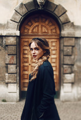 Stunning woman in black coat poses before an old building