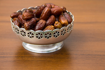 Dates fruit on a silver bowl on wooden table. The Muslim feast of the holy month of Ramadan Kareem