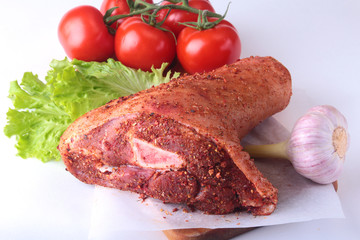 Fototapeta premium Raw pork knuckle and vegetables, garlic, tomatoes spices and lettuce leaves on a cutting board. Selective focus. Ready for cooking.