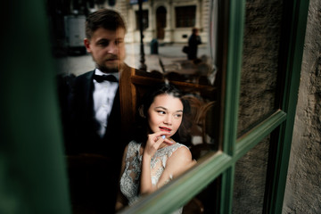 Groom looks at bride from the outside while she sits in the cafe