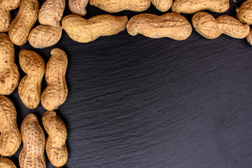 Unclean peanuts lie on a black stone board in the form of a frame, space for text