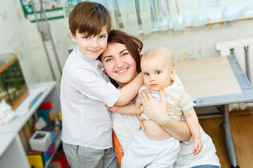Young and happy mother hugs her two beautiful children. Sitting on chair in children room at home