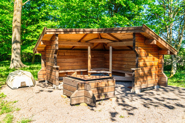 Wooden hiking shelter with lifeboat to the side and a fire pit for cooking and warmth in front. Forest in background.