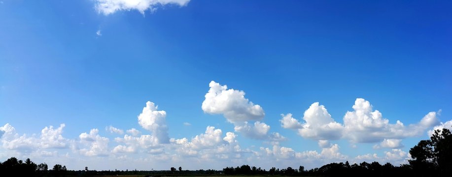 Panorama view of clear blue sky with soft white clouds and sun rays