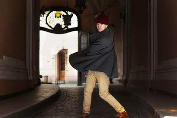 Happy young man whirls his grey coat posing in long corridor