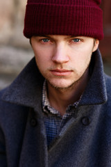 Young man in red hat and grey coat before old house