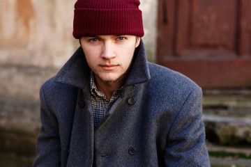 Young man in red hat and grey coat before old house