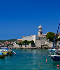 Fototapeta na wymiar Old town Krk with walls and cathedral tower. In the foreground marina and yachts. Mediterranean region, Croatia in Europe