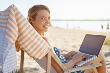 Fototapeta na wymiar Friendly young woman using a laptop at the beach