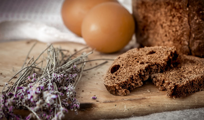 Pieces of rye bread on a wooden kitchen board, two eggs and dry lavender. Simple rustic food.