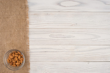 Almonds in a glass bowl and old white wooden table.
