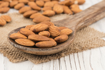 Almonds in a wooden spoon on the old white wooden table.