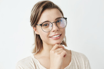 Portrait of young beautiful girl in glasses smiling looking at camera holding hand on chin over...