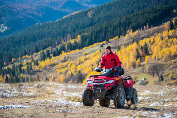 Man is riding up on a atv on a mountain road. Beautiful landscape of mountains woodlands with a variety of color of the trees green, yellow on the background © anatoliy_gleb