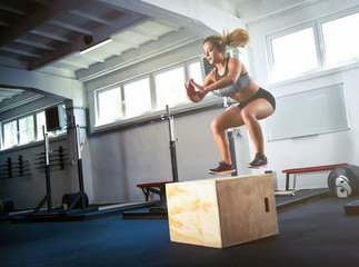 Fitness woman jumping on box training at gym